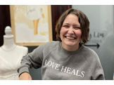 Cassie Wolfe, wearing a sweatshirt that says, “Love Heals,” holds up bags from a successful shopping trip.